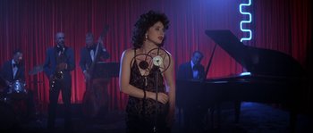 Movie still from “Blue Velvet” (1986), directed by David Lynch – A woman standing in front of a microphone in front of a band; Medium shot, Over the shoulder angle