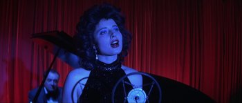 Movie still from “Blue Velvet” (1986), directed by David Lynch – A woman in a black dress singing in front of a red curtain; Close Up shot, High angle