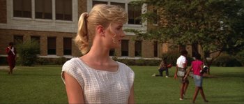 Movie still from “Blue Velvet” (1986), directed by David Lynch – A young blonde haired woman in a white dress is standing in front of a building; Medium shot, Over the shoulder angle