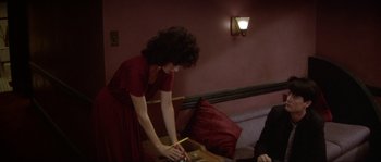 Movie still from “Blue Velvet” (1986), directed by David Lynch – A woman in a red dress is cutting paper with a knife; Medium shot, High angle