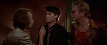 Movie still from “Blue Velvet” (1986), directed by David Lynch – A man in a black shirt and tie holding a tie; Medium shot, Over the shoulder angle