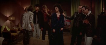 Movie still from “Blue Velvet” (1986), directed by David Lynch – A group of people standing in a living room; Medium shot, Over the shoulder angle