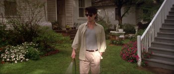 Movie still from “Blue Velvet” (1986), directed by David Lynch – A man in a tan shirt and white pants stands in the grass with a garden hose; Medium shot, Low angle