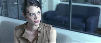 Movie still from “Boarding Gate” (2007), directed by Olivier Assayas – A woman sitting on a couch in front of a window; Close Up shot, Over the shoulder angle
