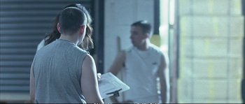 Movie still from “Boarding Gate” (2007), directed by Olivier Assayas – A man and a woman standing next to each other in a room; Medium shot, Over the shoulder angle