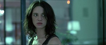 Movie still from “Boarding Gate” (2007), directed by Olivier Assayas – A young woman with long dark hair wearing a black tank top; Close Up shot, Over the shoulder angle