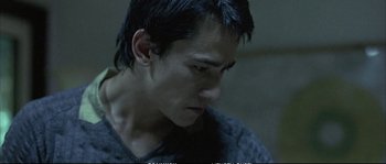 Movie still from “Boarding Gate” (2007), directed by Olivier Assayas – A young man looking down while wearing a sweater; Close Up shot, High angle