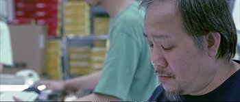 Movie still from “Boarding Gate” (2007), directed by Olivier Assayas – A person sitting at a table; Close Up shot, Low angle
