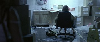 Movie still from “Boarding Gate” (2007), directed by Olivier Assayas – A person sitting in a chair in a room; Wide shot, High angle