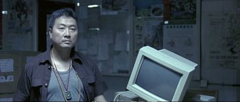 Movie still from “Boarding Gate” (2007), directed by Olivier Assayas – A man standing in front of a computer monitor; Medium shot, Over the shoulder angle