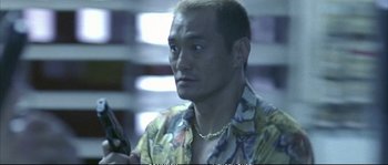 Movie still from “Boarding Gate” (2007), directed by Olivier Assayas – A person wearing a hawaiian shirt; Close Up shot, Low angle