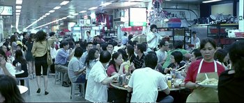 Movie still from “Boarding Gate” (2007), directed by Olivier Assayas – A group of people sitting at a table in a restaurant; Wide shot, High angle