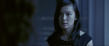 Movie still from “Boarding Gate” (2007), directed by Olivier Assayas – A woman with long black hair is looking at the camera; Close Up shot, Over the shoulder angle