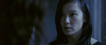 Movie still from “Boarding Gate” (2007), directed by Olivier Assayas – A woman with long black hair is looking at the camera; Close Up shot, Over the shoulder angle