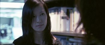 Movie still from “Boarding Gate” (2007), directed by Olivier Assayas – A young woman is standing in front of a bookshelf; Close Up shot, Low angle