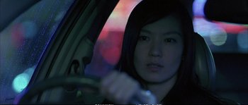 Movie still from “Boarding Gate” (2007), directed by Olivier Assayas – A woman sitting in the driver's seat of a car at night; Close Up shot, Low angle