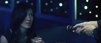 Movie still from “Boarding Gate” (2007), directed by Olivier Assayas – A woman sitting in front of a microphone in a dark room; Close Up shot, Low angle