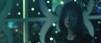 Movie still from “Boarding Gate” (2007), directed by Olivier Assayas – A woman standing in front of a lit up sign; Close Up shot, Low angle