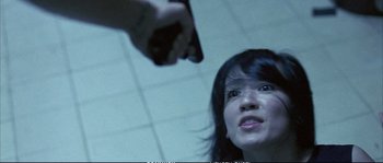 Movie still from “Boarding Gate” (2007), directed by Olivier Assayas – A woman looking up at a person holding a gun; Close Up shot, Low angle