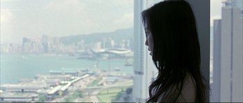 Movie still from “Boarding Gate” (2007), directed by Olivier Assayas – A woman looking out of a window at a city skyline; Medium shot, Over the shoulder angle