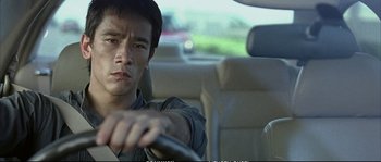 Movie still from “Boarding Gate” (2007), directed by Olivier Assayas – A man driving a car in the middle of the road; Close Up shot, Over the shoulder angle