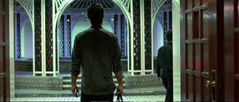 Movie still from “Boarding Gate” (2007), directed by Olivier Assayas – A man holding a cane while standing next to another man; Wide shot, Low angle