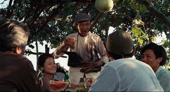 Movie still from “Boat People” (1982), directed by Ann Hui – An old man holding a plate near a group of people; Medium shot, Over the shoulder angle