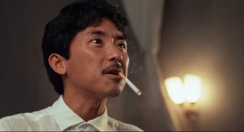 Movie still from “Boat People” (1982), directed by Ann Hui – A man smoking a cigarette while wearing a white shirt; Close Up shot, Low angle
