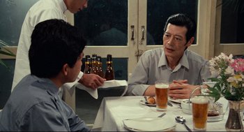 Movie still from “Boat People” (1982), directed by Ann Hui – A man sitting at a table with a tray of beer; Medium shot, Over the shoulder angle