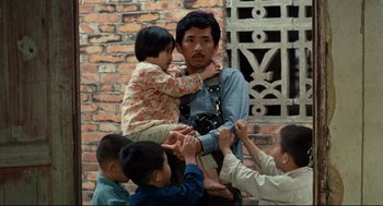 Movie still from “Boat People” (1982), directed by Ann Hui – A man holding a little girl in his arms; Medium shot, Low angle