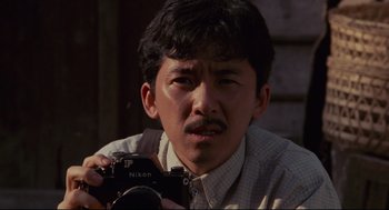 Movie still from “Boat People” (1982), directed by Ann Hui – A man holding a camera in his hands; Close Up shot, Low angle