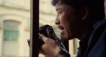 Movie still from “Boat People” (1982), directed by Ann Hui – A man holding an old fashioned camera up to the side of his face; Close Up shot, Low angle