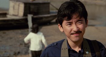 Movie still from “Boat People” (1982), directed by Ann Hui – A man with a beard is smiling for the camera; Close Up shot, Over the shoulder angle