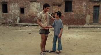 Movie still from “Boat People” (1982), directed by Ann Hui – Two young men standing on a dirt field; Wide shot, Over the shoulder angle