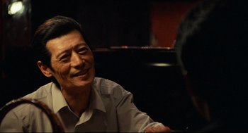 Movie still from “Boat People” (1982), directed by Ann Hui – An older man sitting in front of a piano; Close Up shot, Over the shoulder angle