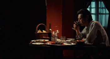 Movie still from “Boat People” (1982), directed by Ann Hui – A man sitting at a dinner table drinking a glass of red wine; Medium shot, Over the shoulder angle