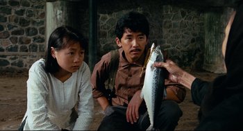 Movie still from “Boat People” (1982), directed by Ann Hui – A man holding up a fish next to two women; Medium shot, High angle