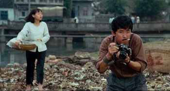 Movie still from “Boat People” (1982), directed by Ann Hui – A man holding a camera while standing next to a woman; Medium shot, Low angle
