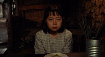 Movie still from “Boat People” (1982), directed by Ann Hui – A girl sitting at a table with a plate of food; Medium shot, High angle