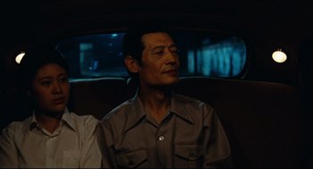 Movie still from “Boat People” (1982), directed by Ann Hui – A man sitting in the back seat of a car; Close Up shot, Over the shoulder angle