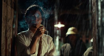 Movie still from “Boat People” (1982), directed by Ann Hui – A man smoking a cigarette while standing in the rain; Close Up shot, Low angle