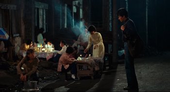 Movie still from “Boat People” (1982), directed by Ann Hui – A group of people sitting around a fire pit; Wide shot, High angle