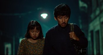 Movie still from “Boat People” (1982), directed by Ann Hui – A man and a woman standing next to each other on a street; Medium shot, High angle