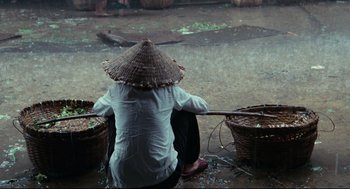 Movie still from “Boat People” (1982), directed by Ann Hui – A person sitting on the ground with baskets of food; Wide shot, High angle