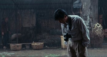 Movie still from “Boat People” (1982), directed by Ann Hui – A man holding a camera while standing in the pouring rain; Medium shot, Low angle