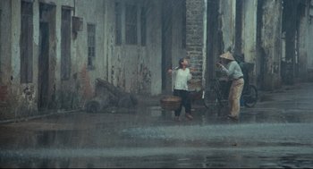 Movie still from “Boat People” (1982), directed by Ann Hui – Two people standing in the rain near a building; Extreme Wide shot, High angle