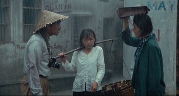 Movie still from “Boat People” (1982), directed by Ann Hui – A woman holding a stick in front of two other people; Wide shot, Over the shoulder angle