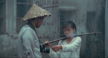 Movie still from “Boat People” (1982), directed by Ann Hui – A man and a woman in the rain with a camera; Medium shot, Over the shoulder angle