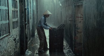 Movie still from “Boat People” (1982), directed by Ann Hui – A man wearing a hat is standing in the rain; Wide shot, High angle