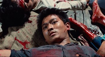 Movie still from “Boat People” (1982), directed by Ann Hui – A young man is laying on the ground with blood on his face; Close Up shot, Overhead angle